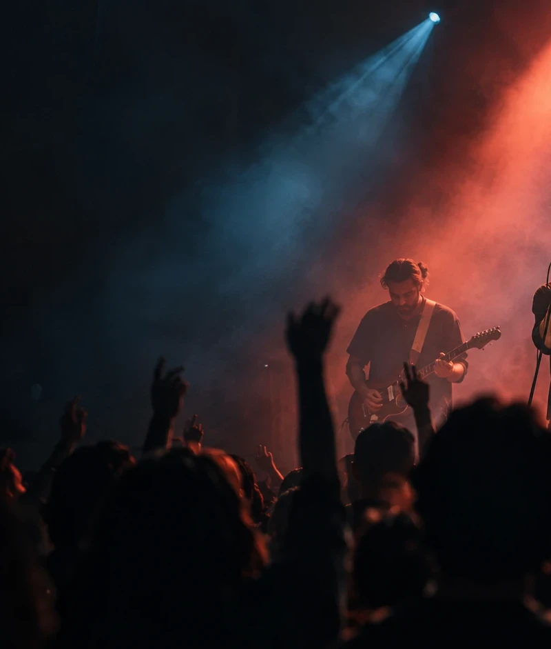 A band on stage under blue and red beams, with the audience in the foreground